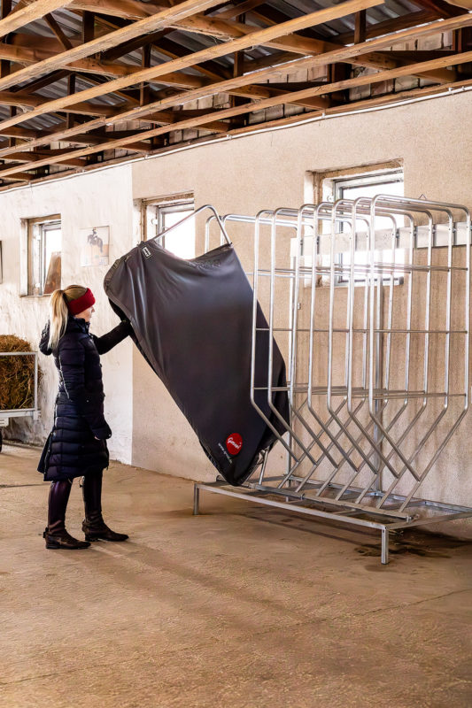 Der Deckenhalter Ergonomic in Anwendung - wie einfach die Nutzung ist, zeigt die Person auf dem Bild indem sie nur eine Hand benutzt um den Halter mit Decke nach oben zu klappen.